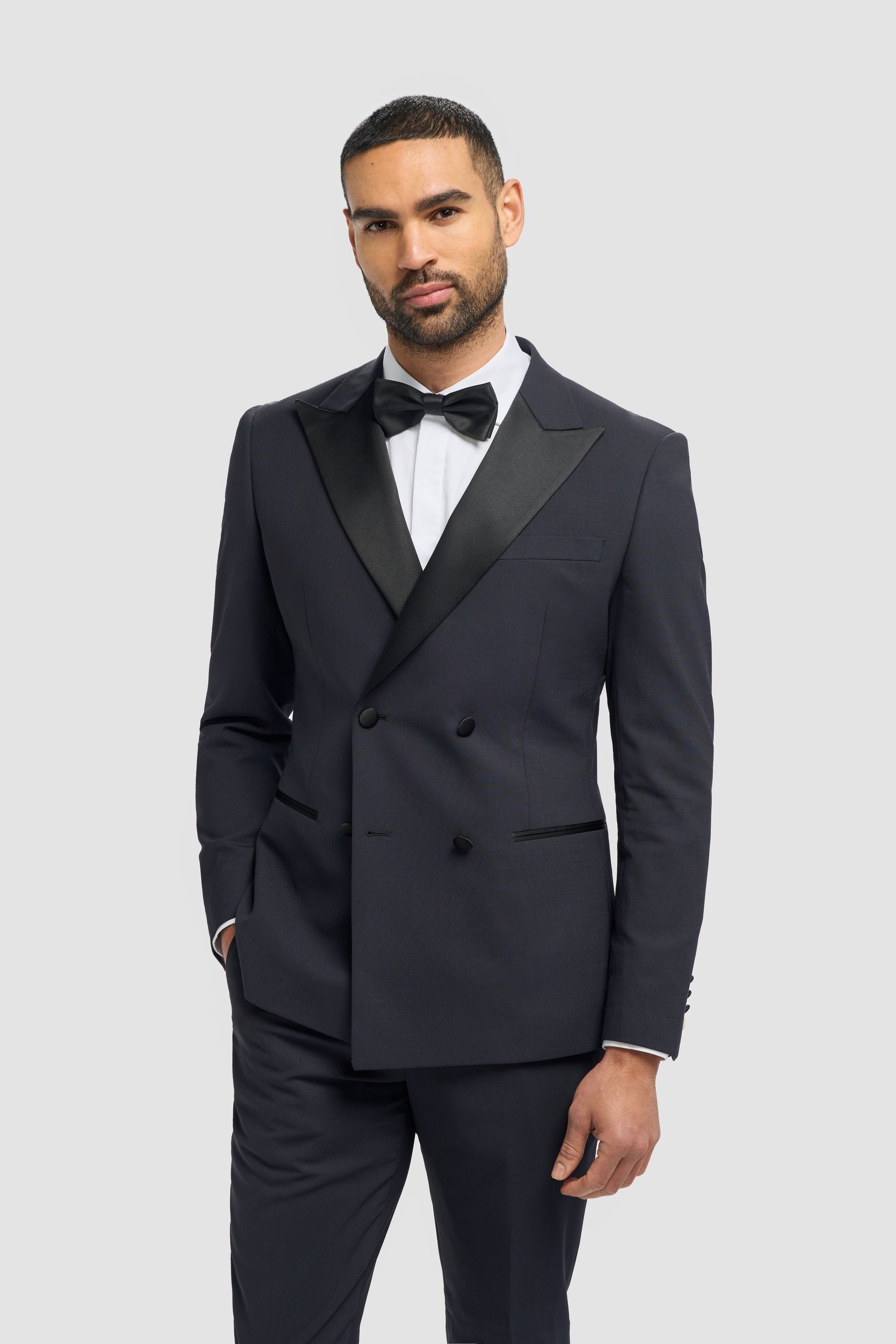 Man wearing a black tuxedo with a white shirt and black bow tie on a light gray background